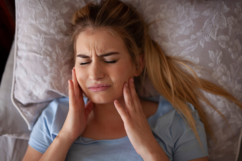 Woman laying in bed experiencing jaw pain.